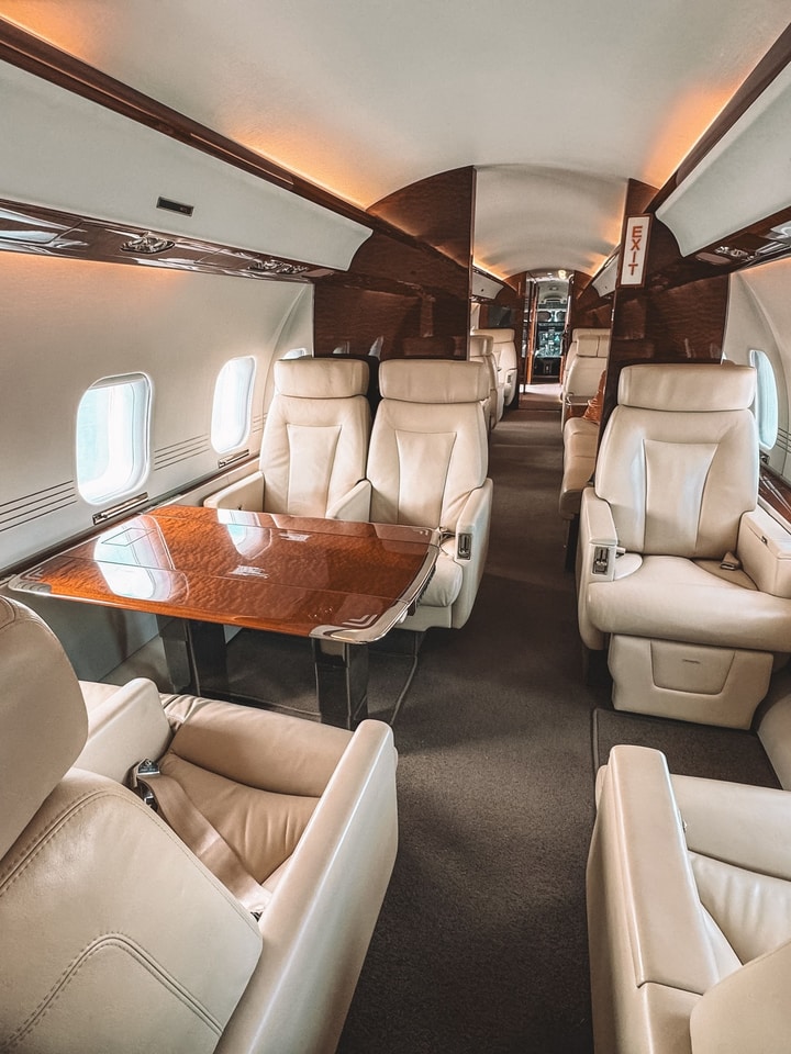 Business jet cabin with light leather seats and a wooden table